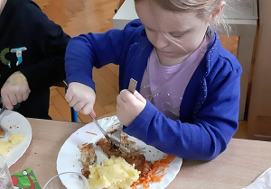 Ania uczy się posługiwania widelcem i nożem podczas posiłku.